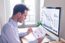 Male business worker in front of a computer monitor at desk holding a chart of financial numbers